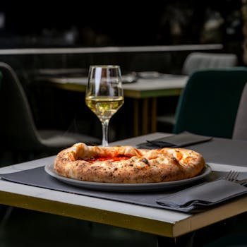 A tempting pizza and glass of white wine on a restaurant patio table, ideal for food enthusiasts.